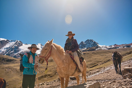 Native guide with horse riding tourist on horseback with traditional clothes dress on hike tour to colorful Rainbow Mountain near Cusco, Peruの写真素材