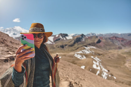 Young girl photographing on phone beautiful landscapes, traveling highly in the mountains on Ausangate Mountain, Peru South Americaの写真素材