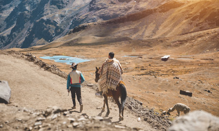 Peruvian Andean man wearing traditional colorful clothing walking up the hill, pulling a horse by the rope in the andean Mountain. Peruの写真素材