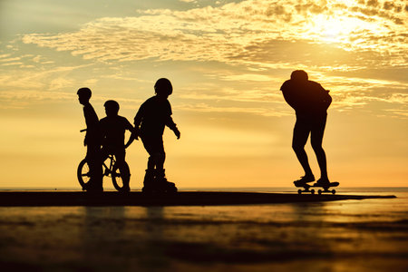Silhouette of young jumping skateboarder riding longboard, summer sunset background. Culture Enjoy...