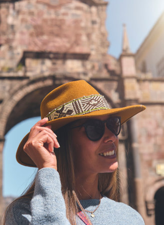 Stepping Into Another World. Historical Tourism Concept. Young woman traveler in brown hat walks through of the Santa Clara Arch in San Francisco square. Cusco, Peru.の写真素材
