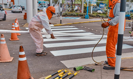 Three men in orange work clothes are painting a crosswalkの写真素材