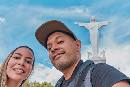 A man and a woman are posing for a picture in front of a statue of Jesus Christ, archs of Acuchimay,...