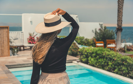 A woman wearing a straw hat stands in front of a poolの写真素材