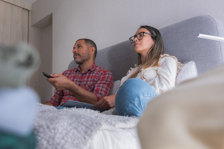 A man and woman are sitting on a bed watching televisionの写真素材