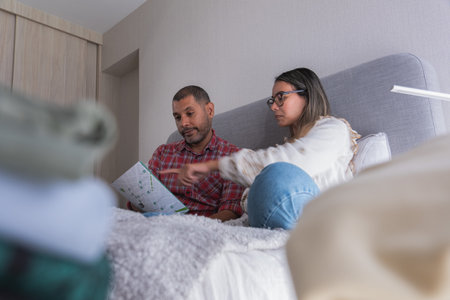 A man and woman are sitting on a bed, looking at a piece of paper. New home concept.の写真素材