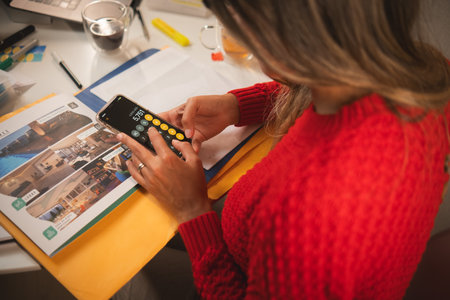 A woman is sitting at a desk with a cell phoneの写真素材