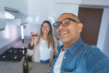 A man and a woman are smiling and holding wine glasses in a kitchen.の写真素材