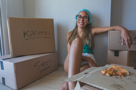 A woman is sitting on the floor next to boxes labeled Kitchen and Shoes. New home concept.の写真素材