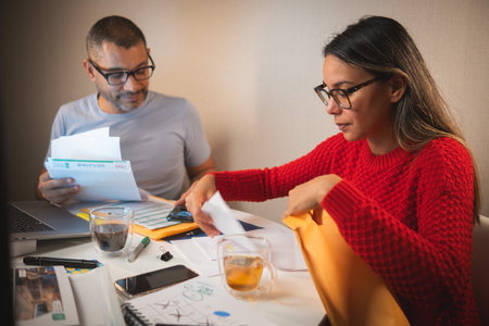 A man and a woman are sitting at a table with papers and a laptop, couple organizing documents.の写真素材