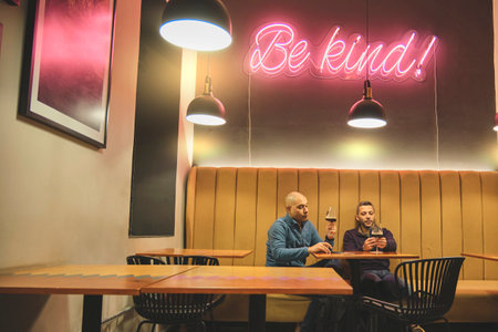 Two men sitting under a neon sign in a craft beer bar