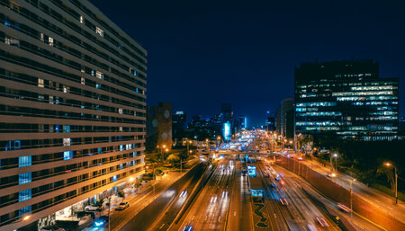 Cars driving on a busy highway next to an illuminated office building at nightの写真素材