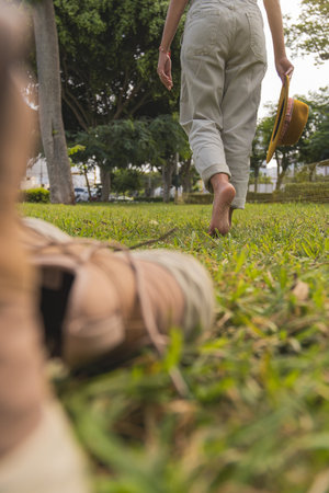 Young woman walking barefoot on grass holding a hat
