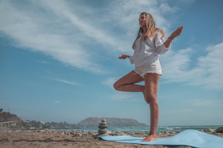 Yoga instructor performing tree pose on beach during summer meditation timeの写真素材
