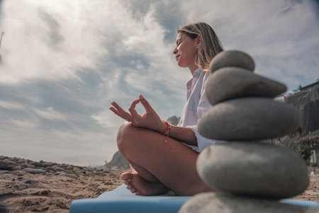 Woman meditating on beach with stack of zen stones during summertimeの写真素材