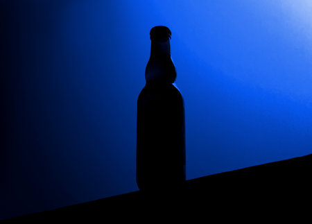 Dark beer bottle silhouette standing on a surface with blue backlightの写真素材