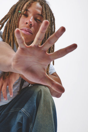 Young man with dreadlocks extending arm and open hand towards viewer in studioの写真素材