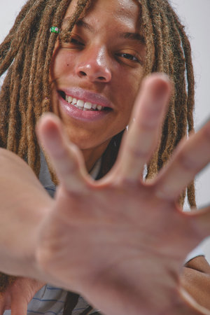 Joyful person with dreadlocks reaching hand forward looking directly at viewerの写真素材