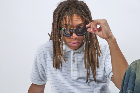 Young man wearing a striped polo shirt poses with dreadlocks and sunglassesの写真素材