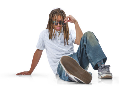 Young man with dreadlocks modeling sunglasses, sitting casually on white backgroundの写真素材