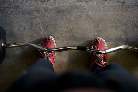 person wearing old red shoes standing above barbellの写真素材