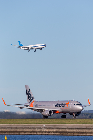Sydney, Australia - May 5, 2014: Jetstar Airways Airbus A320 airliner at Sydney Airport with a China Southern Airbus A330 on approach in the background.のeditorial素材