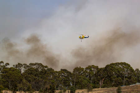 Bundoora, Australia - December 30, 2019: Bell 412 helicopter flying against plumes of smoke while fighting bush fires in Victoria, Australia.のeditorial素材