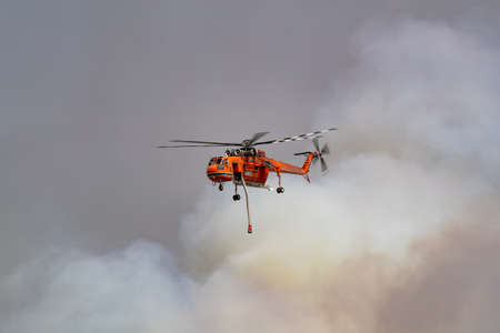 Bundoora, Australia - December 30, 2019: Erickson Air Crane helicopter flying against plumes of smoke while fighting bush fires in Victoria, Australia.のeditorial素材