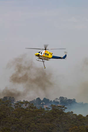 Bundoora, Australia - December 30, 2019: Bell 412 helicopter flying against plumes of smoke while fighting bush fires in Victoria, Australia.のeditorial素材