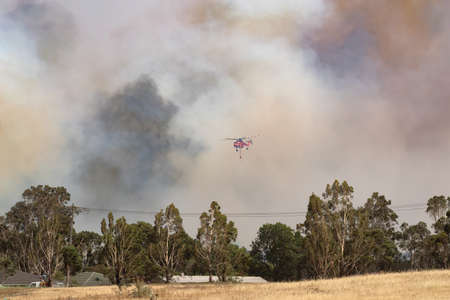 Bundoora, Australia - December 30, 2019: Erickson Air Crane helicopter flying against plumes of smoke while fighting bush fires in Victoria, Australia.のeditorial素材