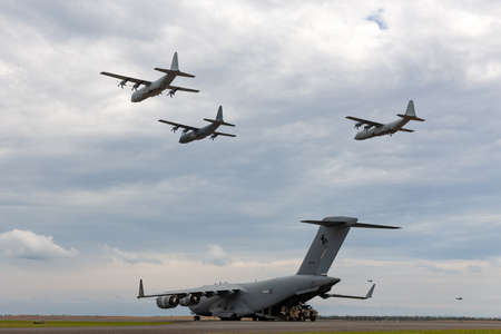 Avalon, Australia - February 27, 2015: Royal Australian Air Force (RAAF) Boeing C-17A Globemaster III Large military cargo aircraft unloading a Bushmaster Armored personnel carrier while three C-130Õs fly overhead.のeditorial素材