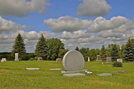 Rolling billowy clouds form over a rural cemetery surrounded by evergreensの写真素材