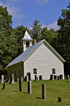 Historic gravemarkers fill the cemetery behind the old white country church.の写真素材