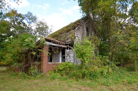 Old dilapidated house falling into ruins is surrounded by bushes and trees.の写真素材
