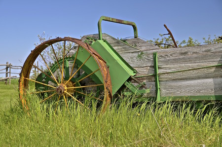 An old wooden manure spreader with steel spoked wheels  is left parked in the long grass