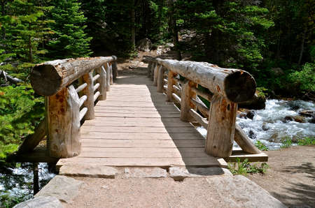 Wooden log bridge spans a mountain stream and leads to a hiking path.の写真素材