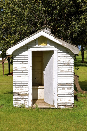 The bench of an old white sided outhouse is open with a chimney birdhouse on the roof.の写真素材