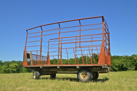 A caged box is parked in a hay field where it receives the bales from a bale thrower.