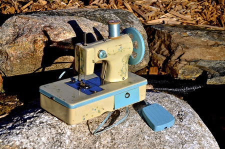 A simple miniature sewing machine with a blue spool of thread.