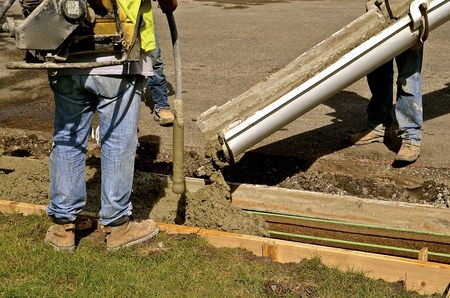Workers ready to work the wet mud ready mix concrete as it slides down a chute in a street curb repair jobの写真素材
