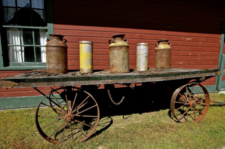 Several old  rusty milk and shotgun cans  are on a platform of an old wooden wagon with steel wheels.の写真素材