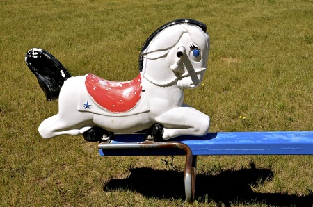 An old plastic horse serves as a seat on the end of a vintage teeter totterの写真素材
