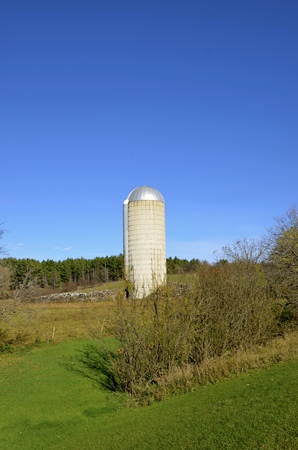 An old tall stave silo stands isolated in a pasture of a former dairy farmの写真素材