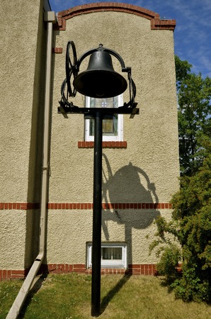 An old  cast iron bell casts it's shadow against a a plaster exterior wall of a church buildingの写真素材