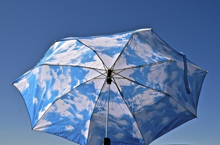 An opened umbrella with a blue sky and cloud pattern blends into the blue outdoor skyの写真素材