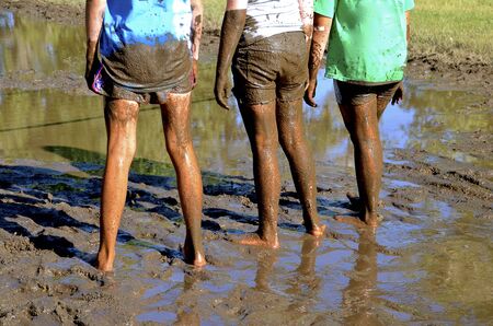 Three teenage girls are lined up at an outdoor mud volleyball court.の写真素材