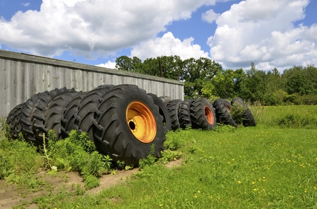 Huge old tractor tires and rims are piled against a weathered wooden fence.の写真素材