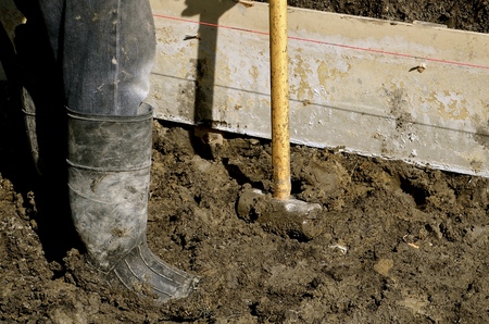 A worker in muddy  boots stands in the mud while building forms to keep wet concrete in place on curb and street constructionの写真素材
