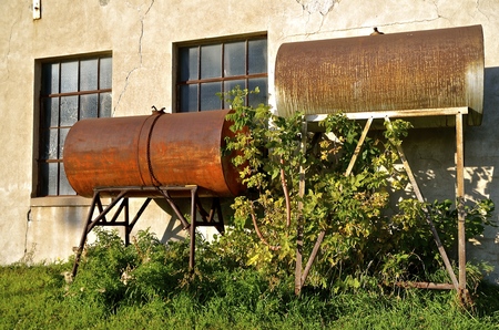 Several old rusty gas tanks are propped on uprights along the wall of a factoryの写真素材