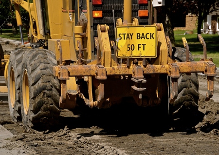 The blade of a road grader moves earth in a road construction street project(rear view)